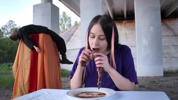 Young woman eating raw liver and lying man behind her — Stock Video