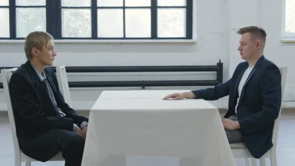 Стрельба двух мужчин, сидящих лицом друг к другу за столом — стоковое видео