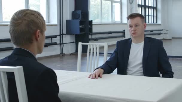 Видео двух мужчин, сидящих лицом друг к другу в ожидании — стоковое видео
