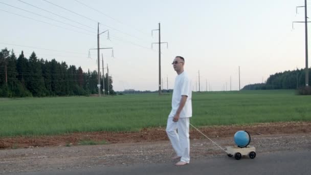 Стрілянина босоніж чоловік тягне дерев'яну розкладку з глобусом — стокове відео