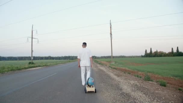 Kuvamateriaalia paljain jaloin mies vetämällä puinen työntökärry maapallon kanssa — kuvapankkivideo
