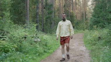 Mutlu sakallı adam yaz parkında yürüyor.