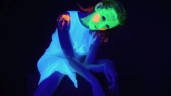 Siedząca przerażająca kobieta z pomalowaną twarzą w świetle ultrafioletowym — Zdjęcie stockowe