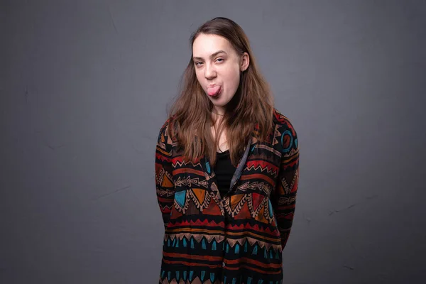 Foto de uma jovem mostrando a língua no fundo cinza — Fotografia de Stock