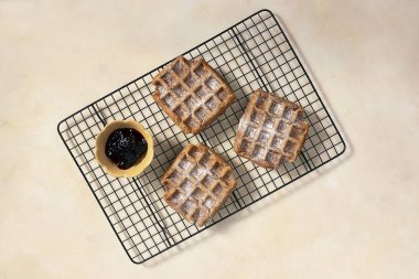 Yukardan taze waffle. En iyi vegan manzarası, reçelli glütensiz waffle ve sarı arka planda pudra şekeri. Lezzetli ev yapımı tatlı.