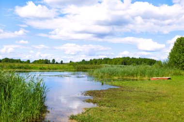 Idyll summer countryside landscape by the river. Boat by the bank, rushes and grass. Wild nature by Biebrza river with beautiful cloudscape reflect in water.