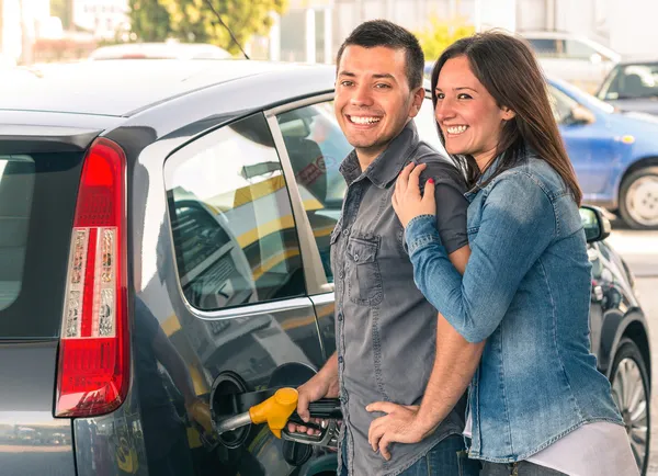 Lyckliga paret på bensinstation pumpa bensin på bensinpump. porträtt av ung man och kvinna man fylla modern bil på bensin tank — Stockfoto