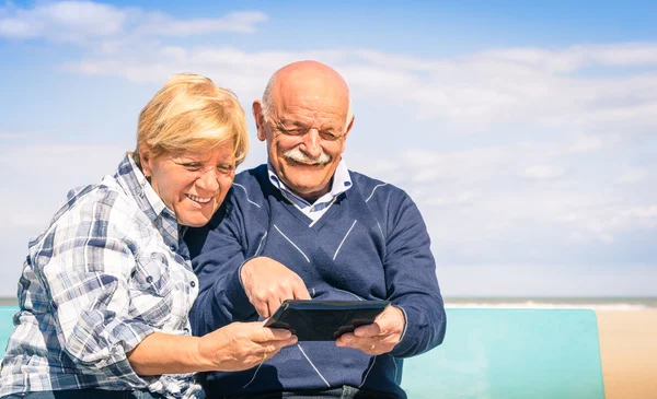Старшая счастливая пара веселится с планшетом на пляже - Портрет мужчины и женщины, взаимодействующих с современными технологиями — стоковое фото