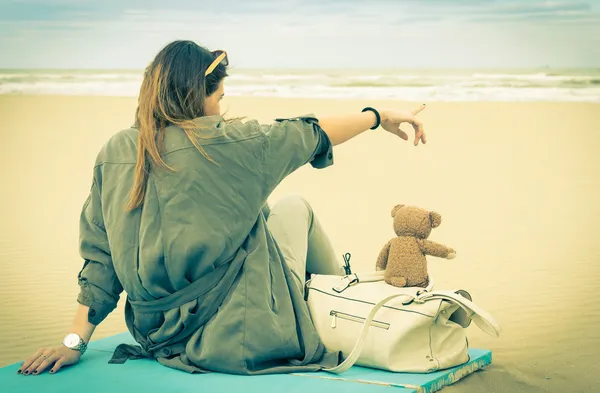 Jovem mulher solteira sentada na praia com seu ursinho de pelúcia olhando para o mar - Vintage retro olhar nostálgico filtrado — Fotografia de Stock