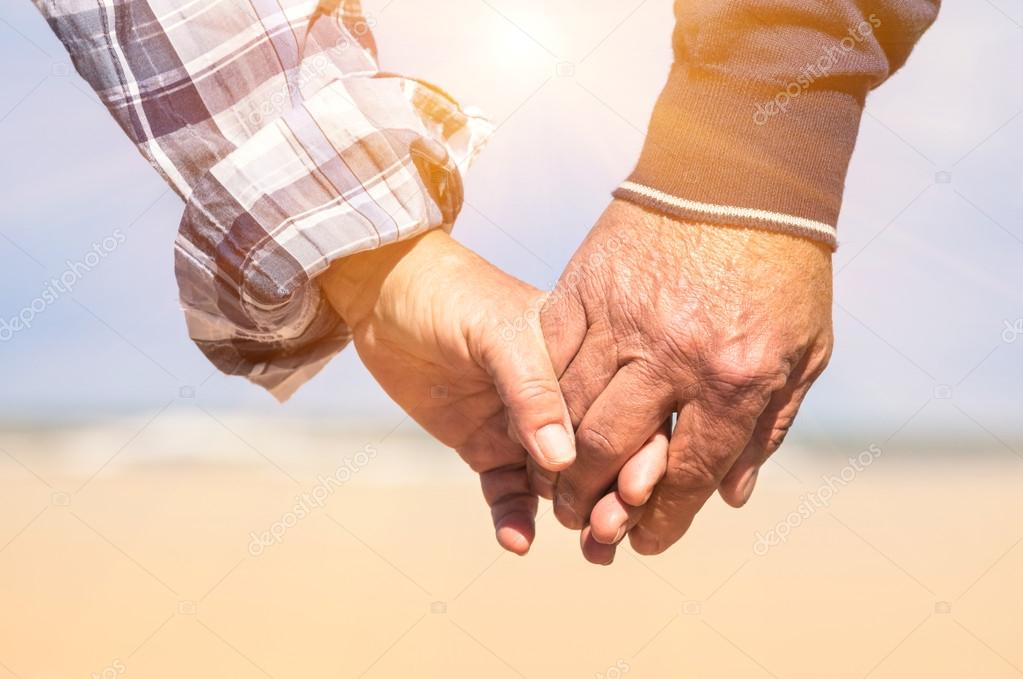 Senior couple in love walking at the beach holding hands in a romantic sunny day - Concept of love and family union
