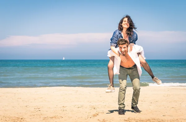 Young couple playing at the beach having fun with a piggyback jump - Happy man and woman at the beginning of a love story — Stock Photo, Image