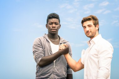 Afroamerican and caucasian men shaking hands in a modern handshake to show each other friendship and respect - Arm wrestling against racism clipart