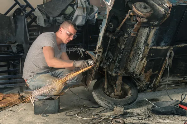 Young mechanical worker repairing an old vintage car body in messy garage