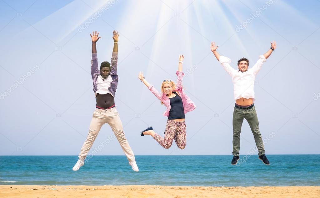 Three multiracial friends jumping at the beach - Concept of happyness and friendship against racism