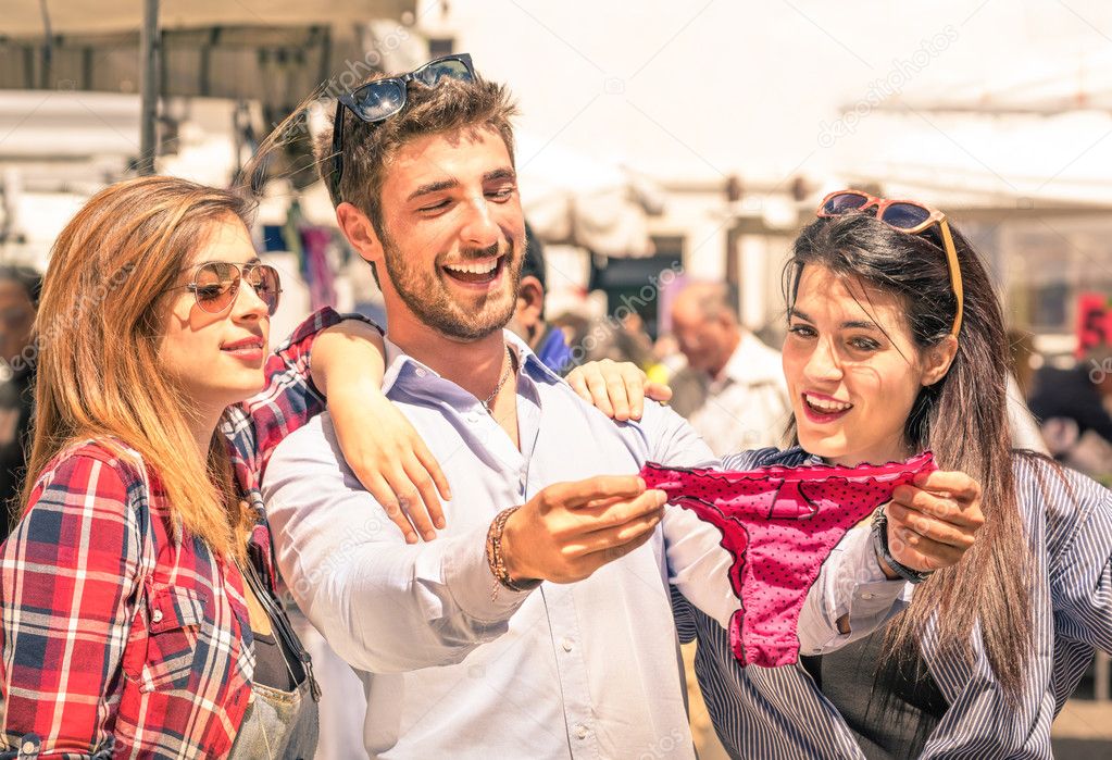 Group of happy young people at the weekly cloth market looking at female underwear - Best friends sharing free time having fun and shopping in the old town in a sunny day