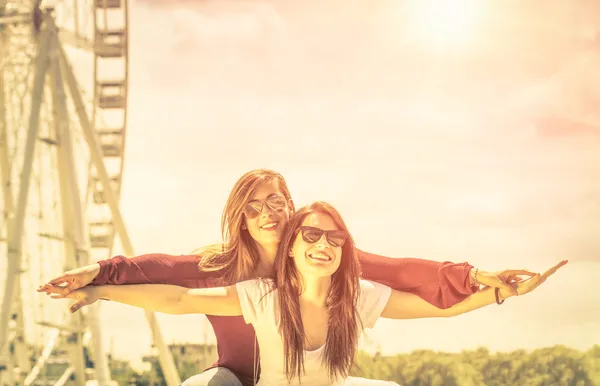 Best friends enjoying time together outdoors at ferris wheel - Concept of freedom and happiness with two girlfriends having fun - Vintage filtered look Stock Image