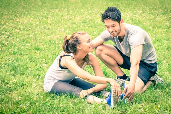 Entraînement de couple heureux dans le parc - Jeune homme et femme pendant l'entraînement d'été et l'activité sportive - Modèles de fitness homme et femme étirant les muscles des jambes après la course - look filtré vintage — Photo