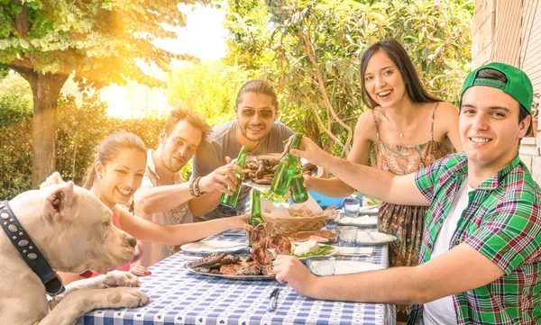Gruppe glücklicher Freunde beim Essen und Anstoßen am Gartengrill - Konzept des Glücks mit jungen Menschen zu Hause, die gemeinsam essen Stockbild