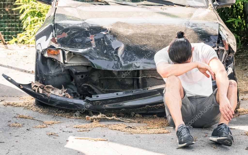Desperate man crying on his old damaged car after a crash accident