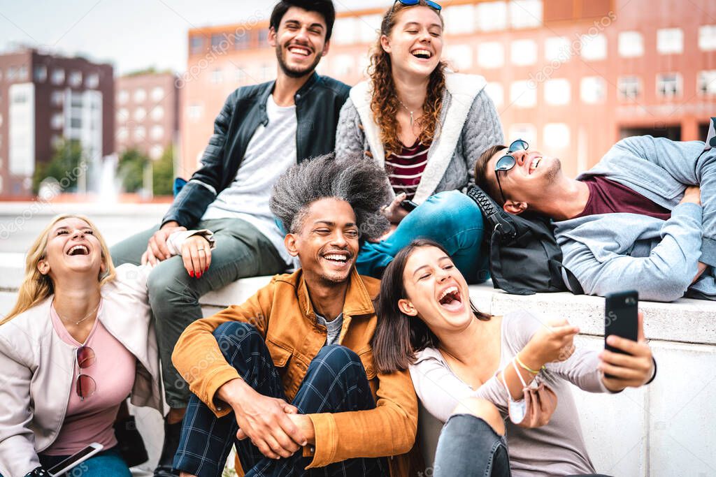 Happy milenial friends having fun with mobile phone at campus college yard - Joyful guys and girls spending tech time together at university lecture break - Warm bright filter with focus on lower guy