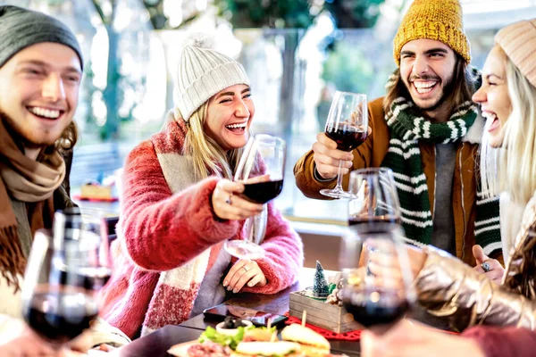 レストランパティオで赤ワインを味わう若い友人 冬服を着てワイナリーバーで一緒に楽しむ幸せな人々 左の女性に焦点を当てた明るいフィルターでのダイニングライフスタイルのコンセプト — ストック写真