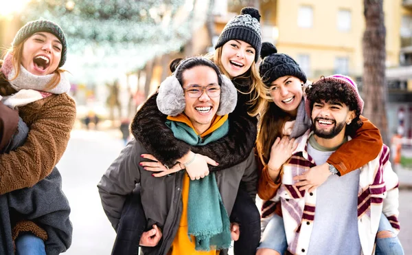 ピギーバック移動の冬の旅行の場所を歩く幸せな多文化の友人 屋外で一緒に楽しむ幸せな男と女の子との日常生活スタイルの概念 暖かいバックライトフィルター — ストック写真