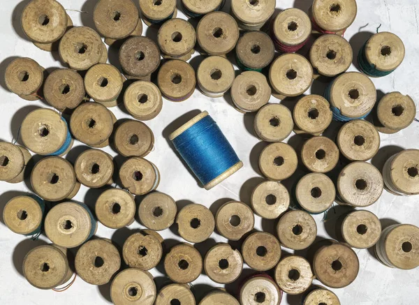 Vintage threads wound on wooden spools are made up around one bobbin of blue threads on a gray background, top view. Retro style concept