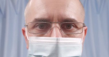 A masked doctor wears glasses. Glasses fog up from breathing. Close-up.