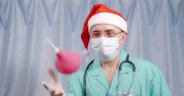 Veselý lékař v klobouku Santa Claus hraje s klystýrem a gesta schvaluje postup. — Stock video