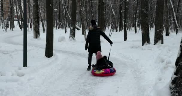 母亲和女儿在室外的冬季森林里滑雪筒上滑行 女儿和妈妈在冬园玩 — 图库视频影像