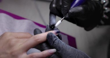 Nail master remove nail polish in beauty saloon with electric file nail. Manicure master in  black gloves removes gel polish from nails using a cutter. Hardware manicure close-up. Shellac nail coating