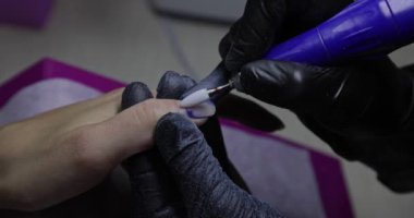 Nail master remove nail polish in beauty saloon with electric file nail. Manicure master in  black gloves removes gel polish from nails using a cutter. Hardware manicure close-up. Shellac nail coating