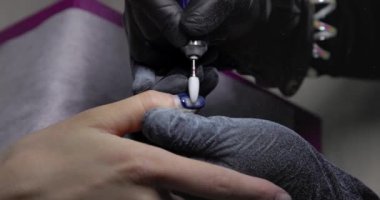 Nail master remove nail polish in beauty saloon with electric file nail. Manicure master in  black gloves removes gel polish from nails using a cutter. Hardware manicure close-up. Shellac nail coating