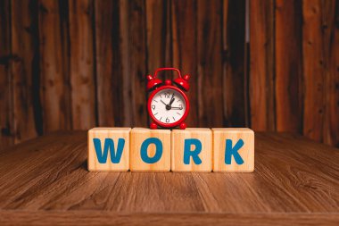 The word work written in English on wooden blocks with a red clock in the image composition. Close up photo.