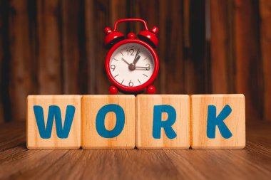The word work written in English on wooden blocks with a red clock in the image composition. Close up photo.