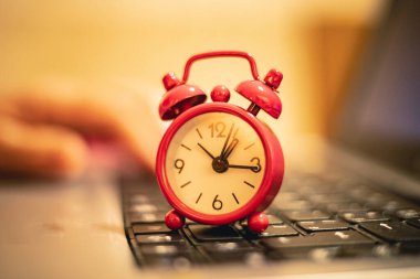 Red clock on the background of laptop keyboard, close-up view