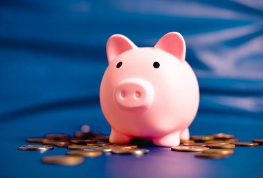 A piggy bank on its side in close-up photo with coins and a blue background. Saving money, finance and economy concepts.