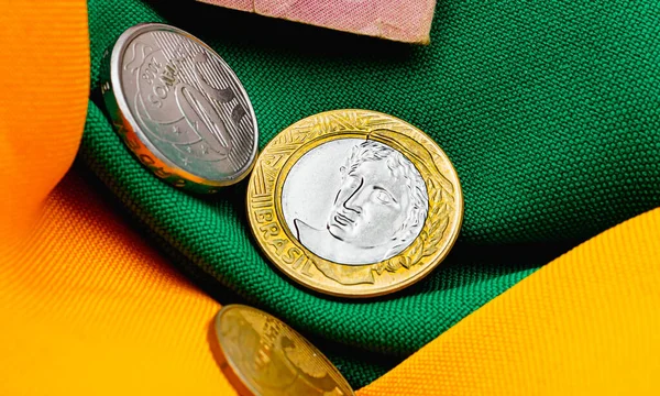 Real - the Brazilian currency. A 1 Real coin and a 50 cent coin in closeup photo. Background in green and yellow reminiscent of the colors of the Brazilian flag. Brazilian economy.