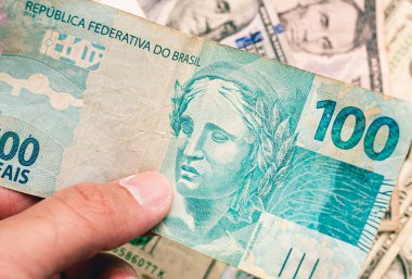 A man holding a Brazilian Real note worth 100 Reais. Brazilian economy and finance.