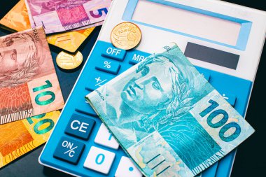Blue calculator, Brazilian Real bills with coins on dark table background. Brazilian economy and finance
