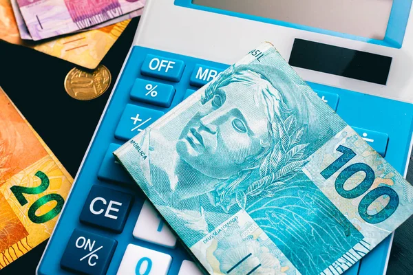 Blue calculator, Brazilian Real bills with coins on dark table background. Brazilian economy and finance