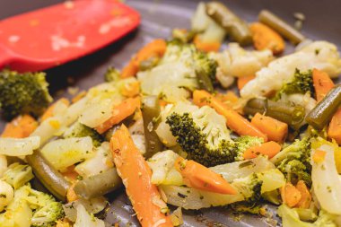 Vegetables sauted inside a frying pan in closeup photo. Broccoli, carrots, green beans and cauliflower.