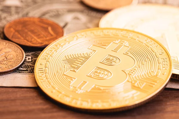 Golden Bitcoin coins and a US coins on a wooden furniture in macro photography. Cryptocurrency, payment method and risk.