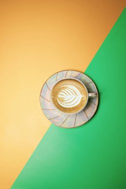 Kahve ve kremalı fincan yeşil-sarı arka planda taç yaprağı şeklinde.