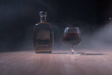 Karanlık bir arka planda konyaklı bardak ve dumanın içinde