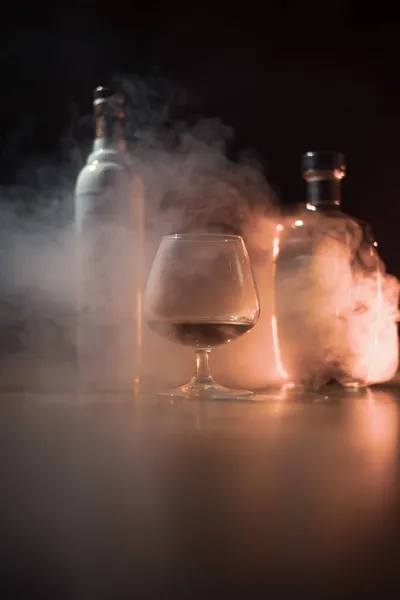 Ett glas konjak på en mörk bakgrund med rök — Stockfoto