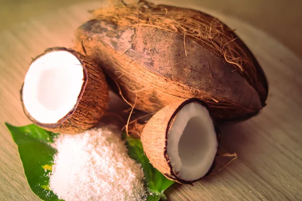 Half coconut and coconut milk with coconut powder on wooden table, coconut powder on green leaf,coconut milk ,selective focus on subject,