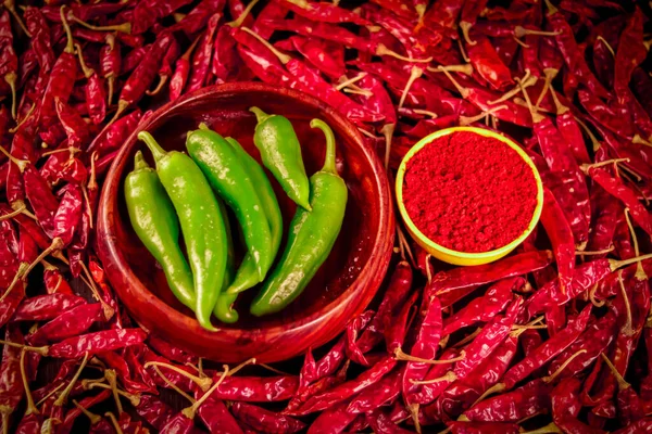 Chili powder with green chillies is on the table and dried red chillies are falling from above,hot dried chili peppers on wooden table