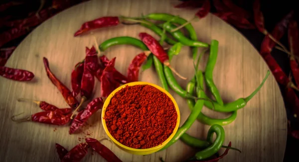 There are dried chillies and blue and red chillies on the table with chili powder is falling from above, yellow bowl in chili pepper powder close up view