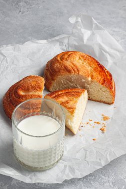 Gri arka planda şekerli kalp şeklinde taze pişmiş beyaz ekmek. Yanında bir bardak süt var..